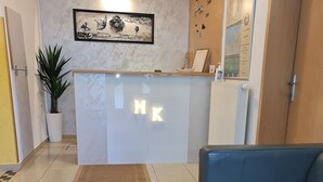 Un mostrador de recepción con letras iluminadas 'HK', una planta en maceta, una obra de arte enmarcada y un sofá de cuero azul.