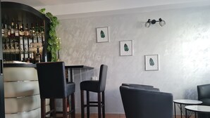 Zona de bar con una barra curva, sillas de cuero negro y una planta en maceta. En la pared, hay obras de arte con hojas enmarcadas y una pequeña mesa redonda con estructura metálica.