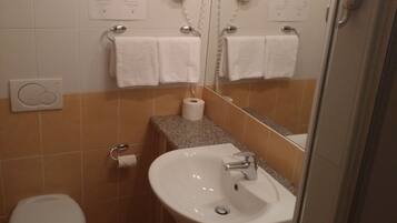 A bathroom with a toilet, sink, and a mirror. There are towels hanging on a rack, and a paper towel dispenser is visible.