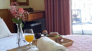 Ett hotellrum med en säng, ett nattduksbord med ett glas apelsinjuice, en hoprullad handduk, en vas med blommor och ett frukostbricka med en smörgås.