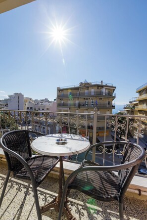 Un balcón con una mesa redonda y dos sillas de mimbre, con vista a un paisaje urbano de edificios y cielo despejado.