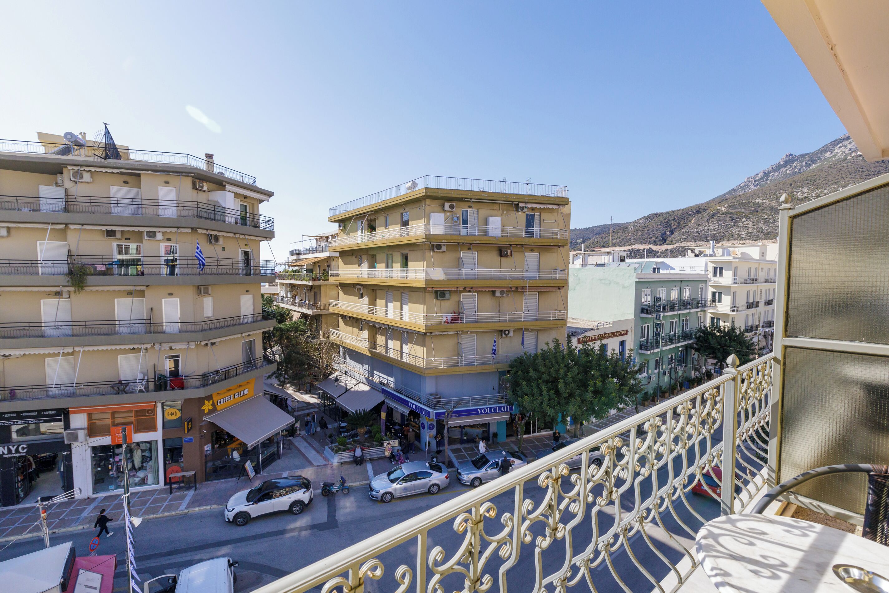 A multi-story building with balconies, a coffee shop, and parked cars on the street.