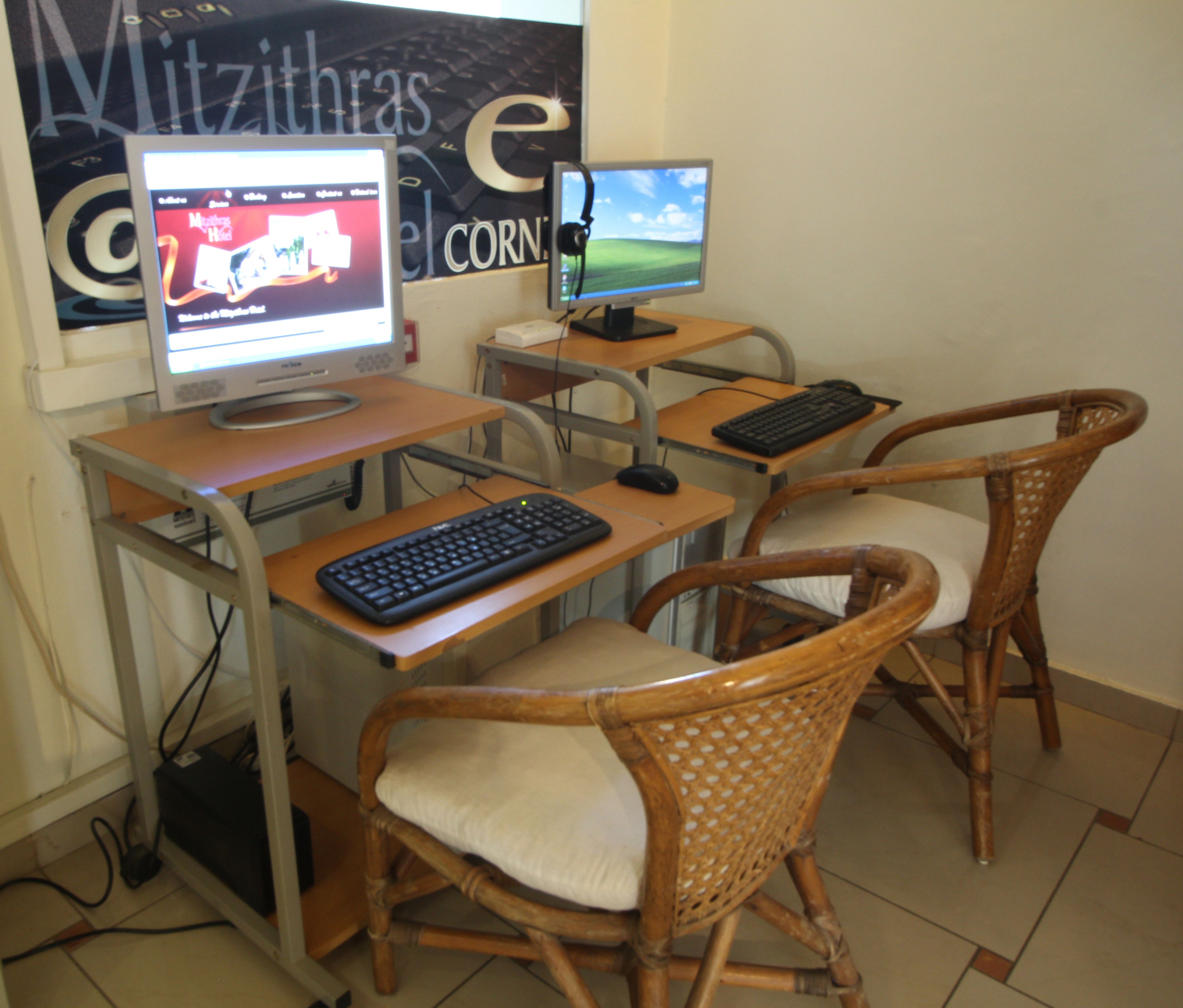 A computer desk with two monitors, a keyboard, and two wicker chairs.