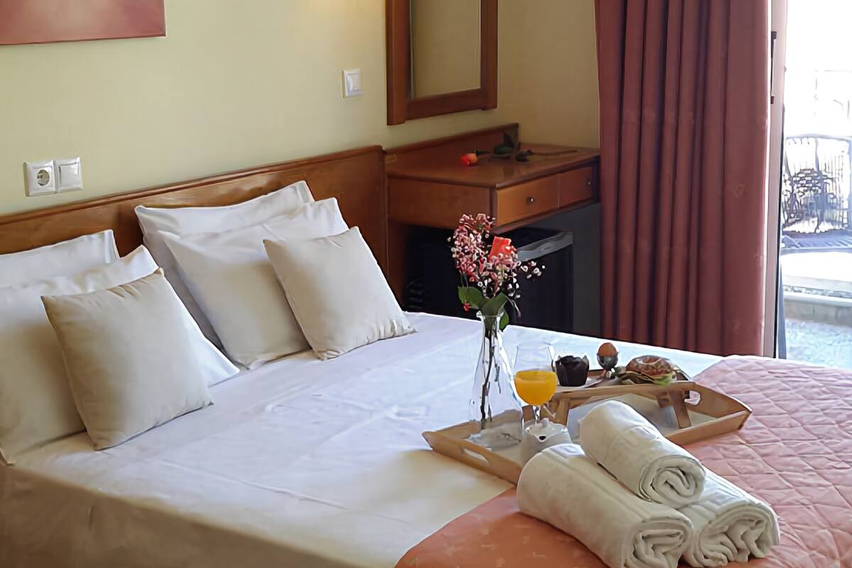 A hotel room with a large bed, a bedside table with a lamp, a mirror, and a window with curtains.