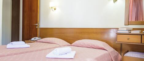 Habitación de hotel con dos camas, cabecero de madera, mesita de noche con lámpara, espejo y cómoda pequeña.