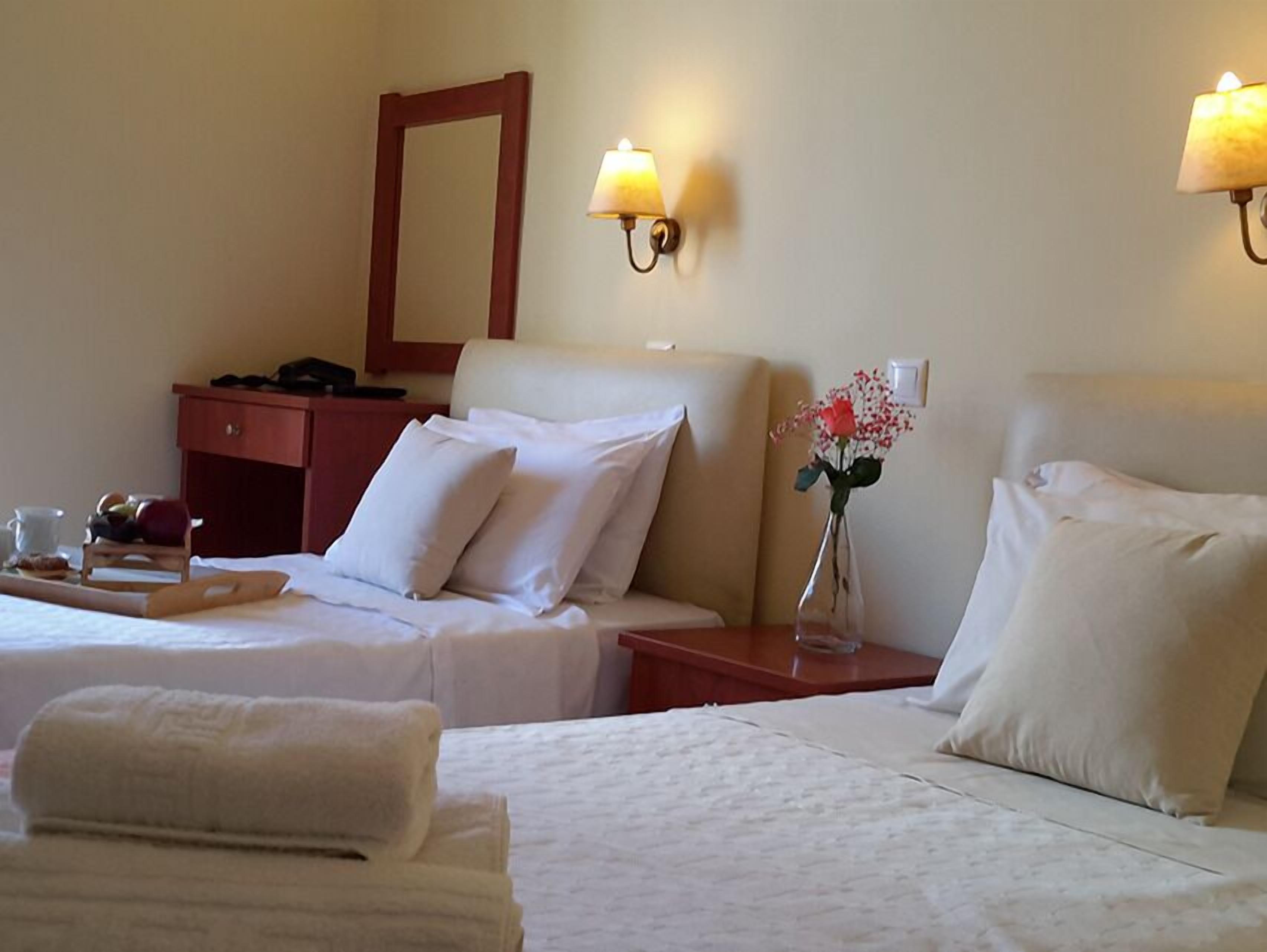 A hotel room with two beds, a nightstand, a dresser, a mirror, and wall sconces.