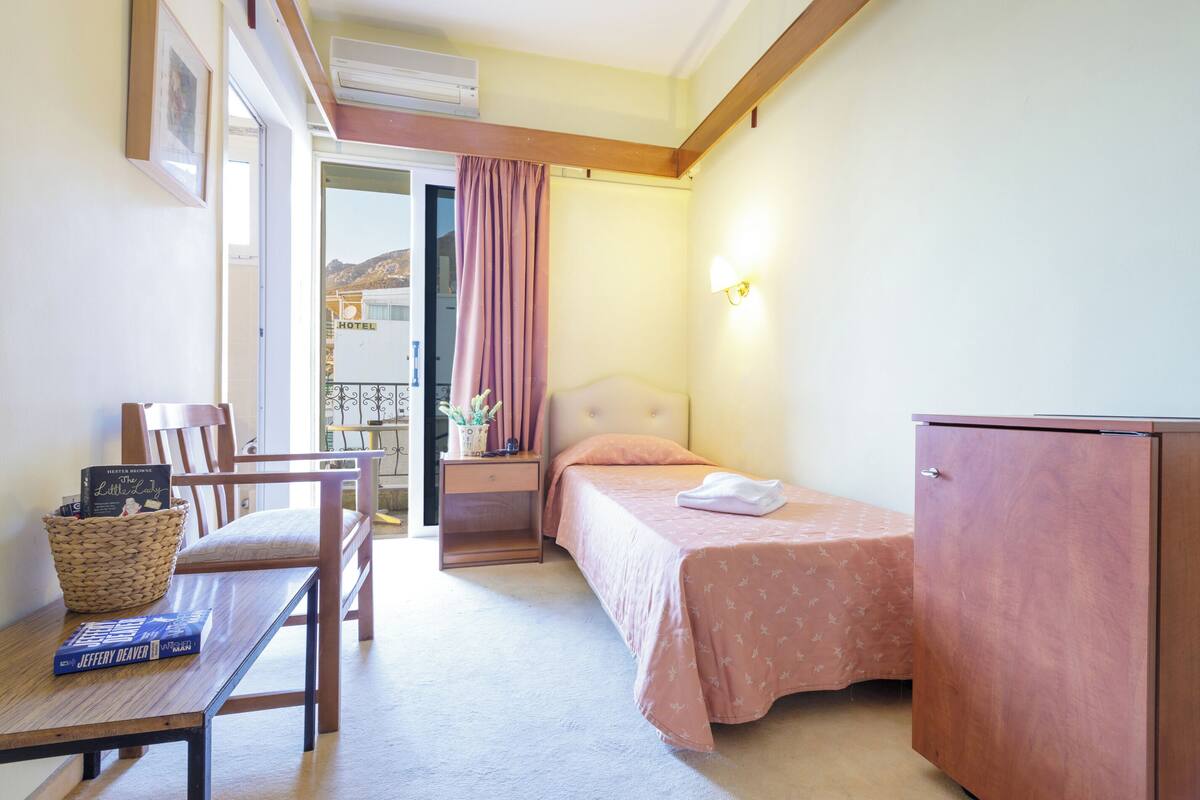 A hotel room with a bed, a desk with a chair, a small table, a cabinet, and a window with curtains.
