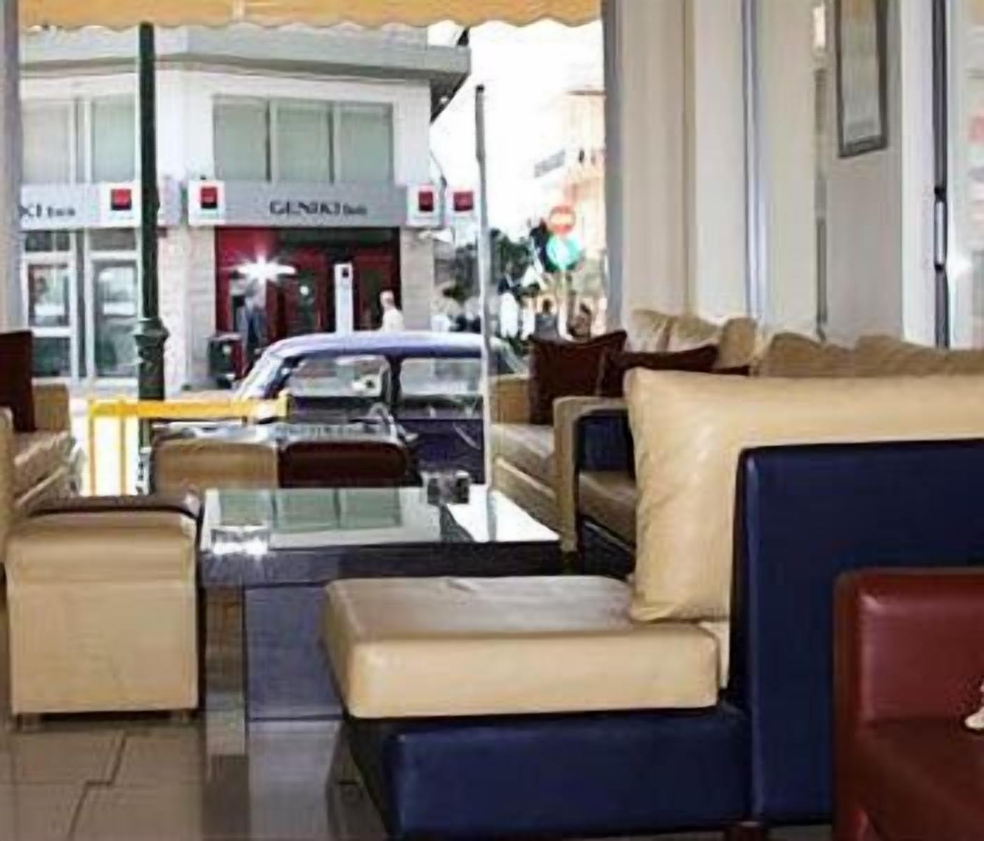 A hotel lobby with a seating area, a glass coffee table, and a view of the street outside.