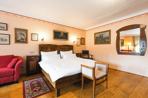 Un dormitorio con una cama de madera, un sillón rojo, una mesita de noche de madera y un espejo en la pared.