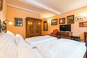 Una habitación de hotel con dos camas, un armario de madera, un televisor y cuadros en la pared.