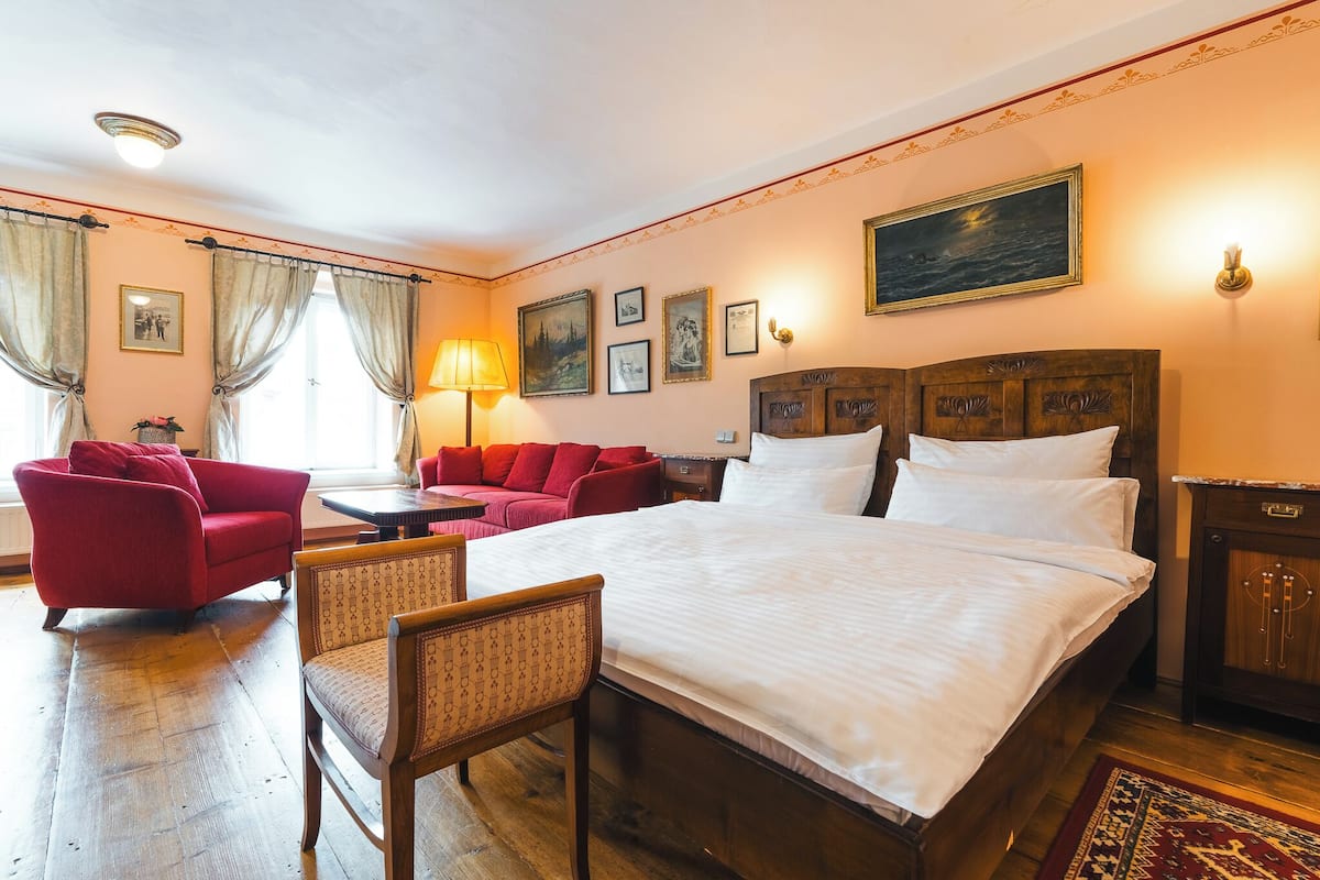 A hotel room with a large bed, a red sofa, a wooden chair, and a small table.
