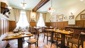 Un comedor con mesas y sillas de madera, una araña y cuadros en las paredes.