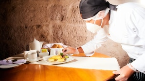 A chef preparing food at a wooden table with a rustic wall in the background.