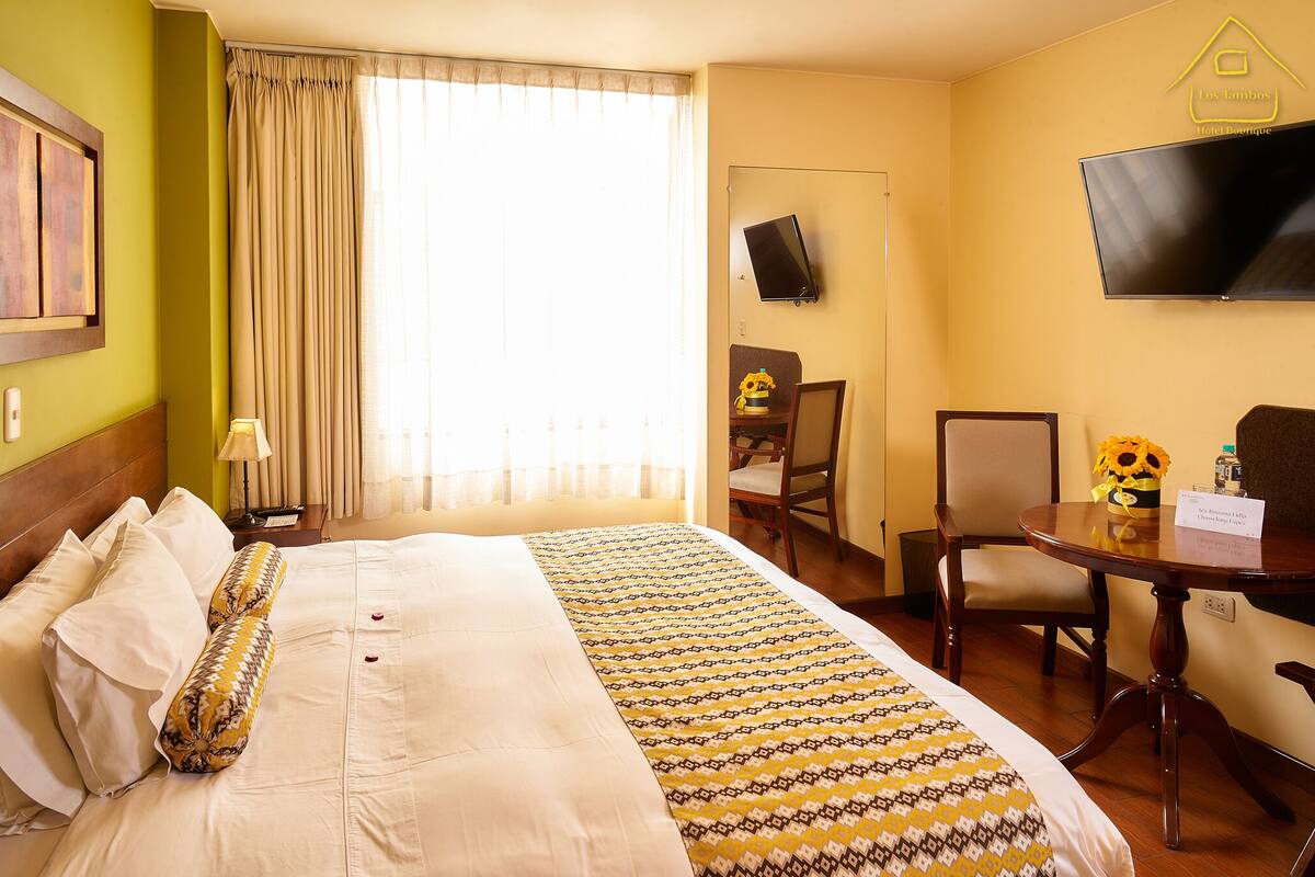 A hotel room with a large bed, a desk, a chair, a television, and a window with curtains.