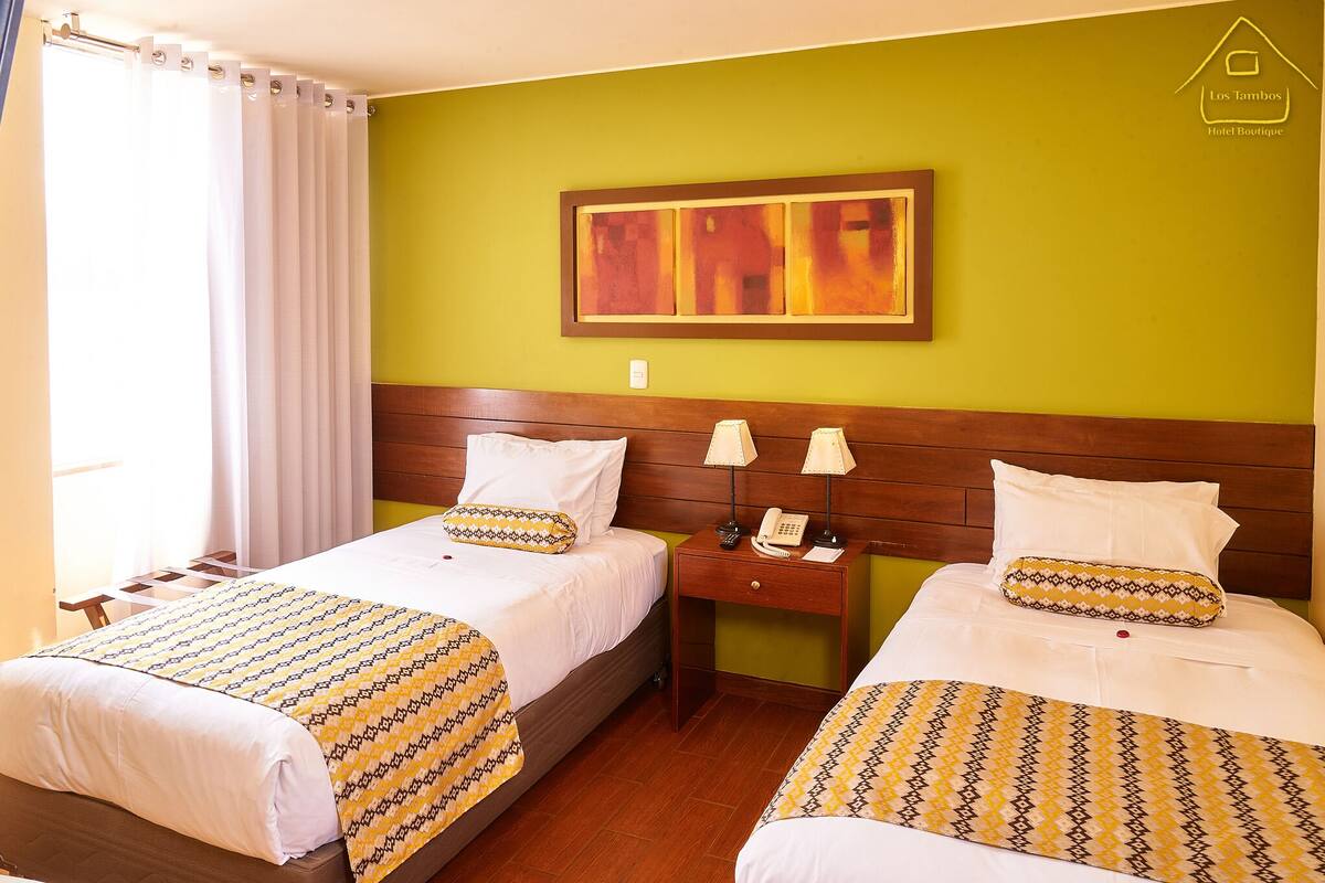 A hotel room with two beds, each with patterned bedding, a wooden headboard, a nightstand with a telephone, and a painting on the wall.