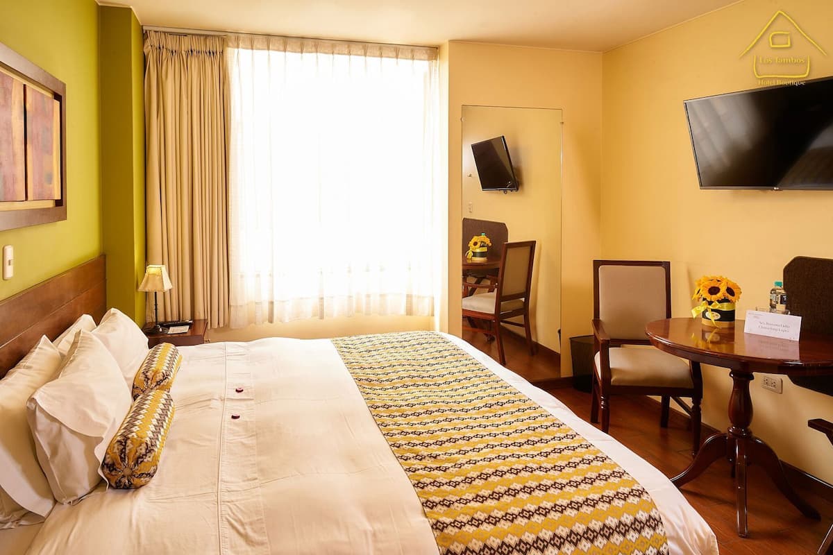 A hotel room with a bed, a desk, a chair, a television, and a window with curtains.