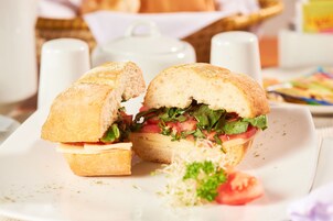 A sandwich on a white plate with a basket and salt shakers in the background.