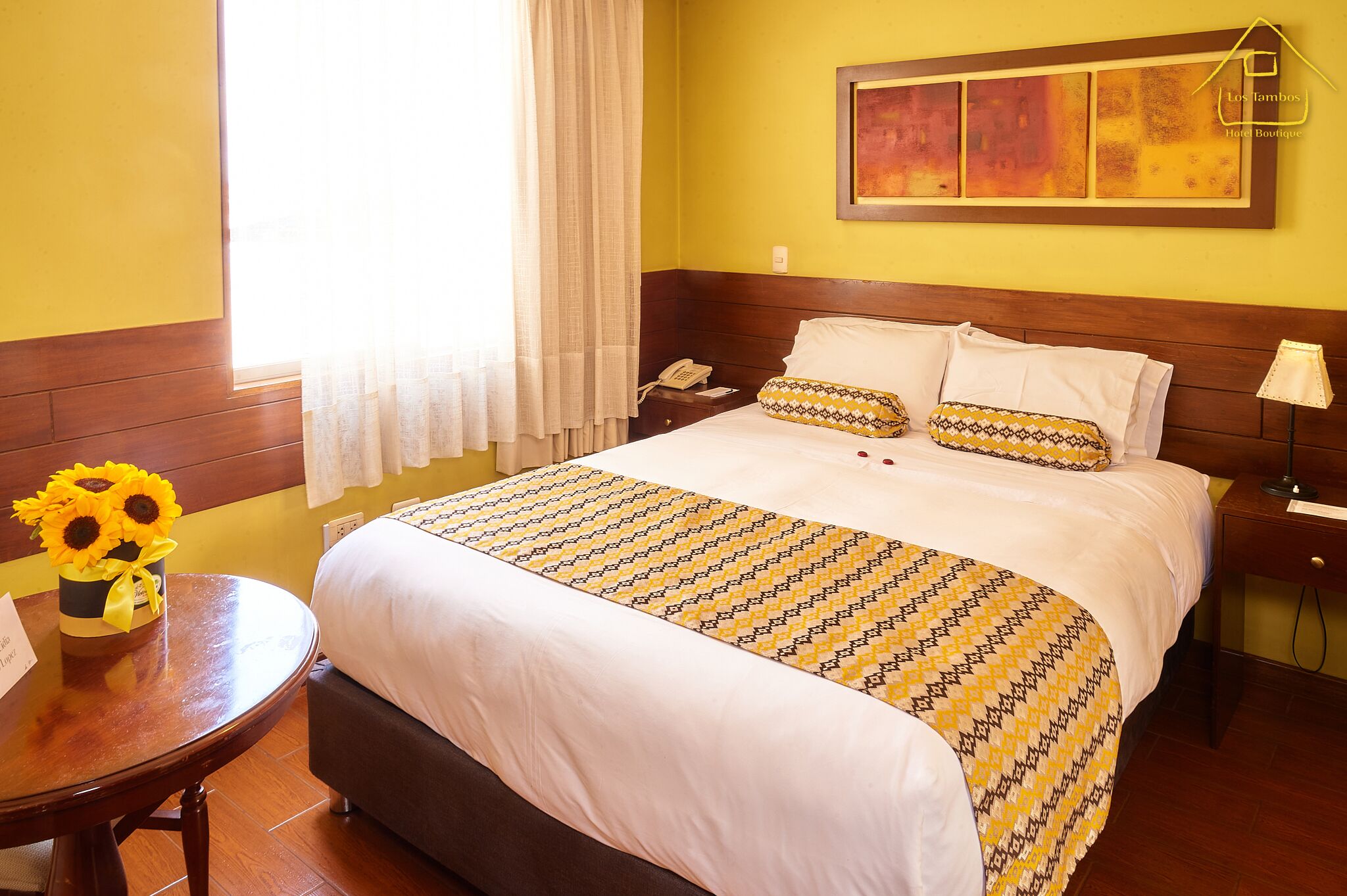 Habitación de hotel con cama, mesita de noche con lámpara, una silla y ventana con cortinas.