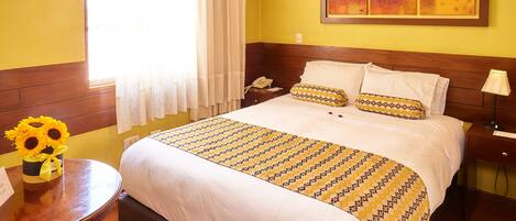 Habitación de hotel con cama, mesita de noche con lámpara, una silla y ventana con cortinas.