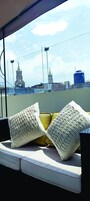 Asiento junto a la ventana con dos almohadones, vista a una torre de iglesia y una torre de agua azul.