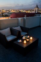 Una terraza en la azotea con mobiliario de mimbre, una mesa con velas y vistas a la ciudad.