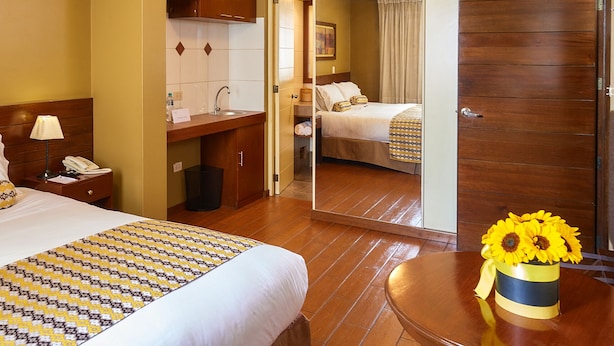 A hotel room with a bed, bedside table, lamp, and a small table with a vase of sunflowers.