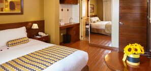 A hotel room with a bed, bedside table, lamp, and a small table with a vase of sunflowers. - Los Tambos - Boutique (Arequipa)
