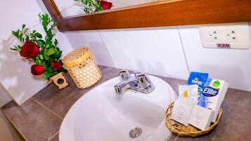 Un baño con lavamanos blanco, un espejo y una cesta con artículos de aseo.