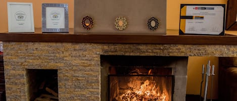 Una chimenea encendida, certificados enmarcados y un reloj en la pared.