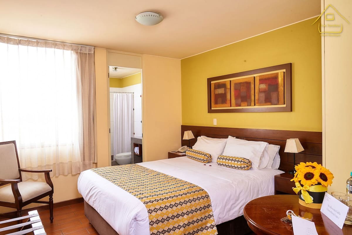 A hotel room with a bed, a chair, a table, and a painting on the wall.
