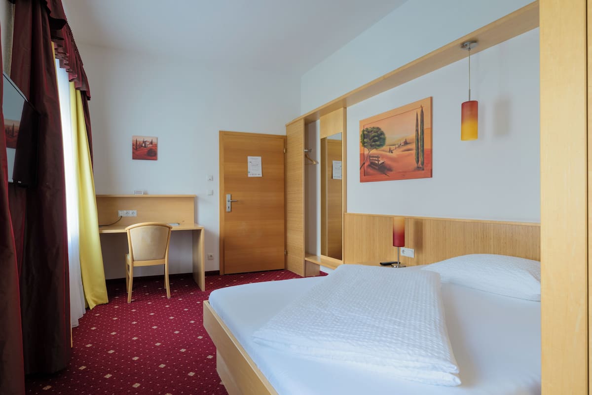 A hotel room with a bed, a desk, a chair, and a wardrobe.