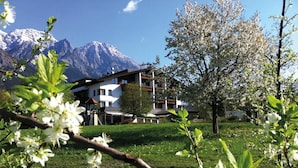 A hotel with a mountain backdrop, a garden with blooming flowers, and a clear sky.