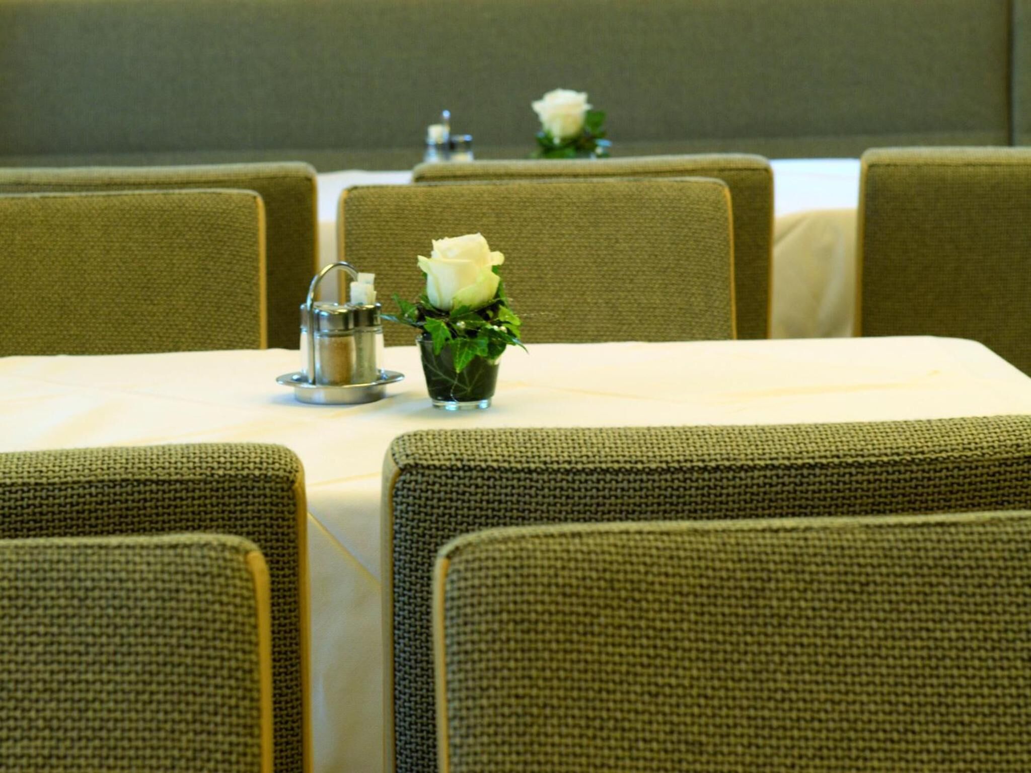 Una sala conferenze con un tavolo apparecchiato per una riunione. Ci sono sedie attorno al tavolo, un piccolo vaso con una rosa bianca e un teiera d'argento sul tavolo.