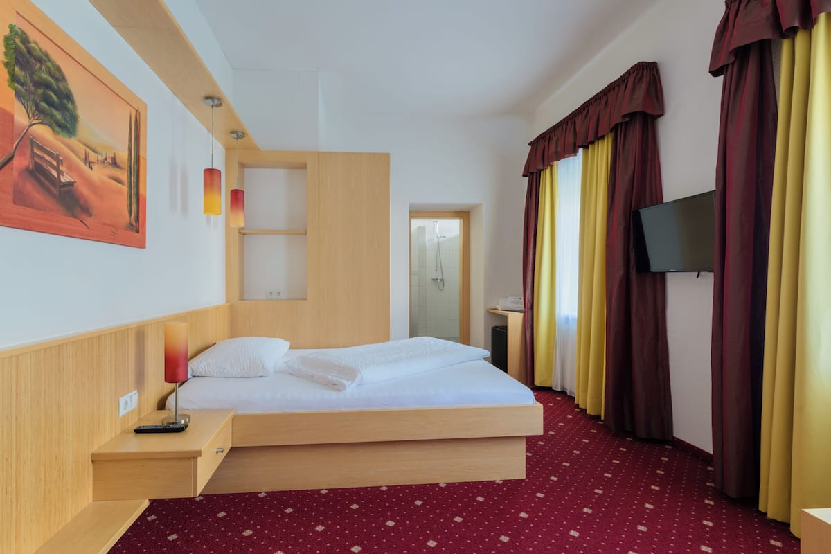 A hotel room with a bed, a nightstand, a TV, and a painting on the wall.