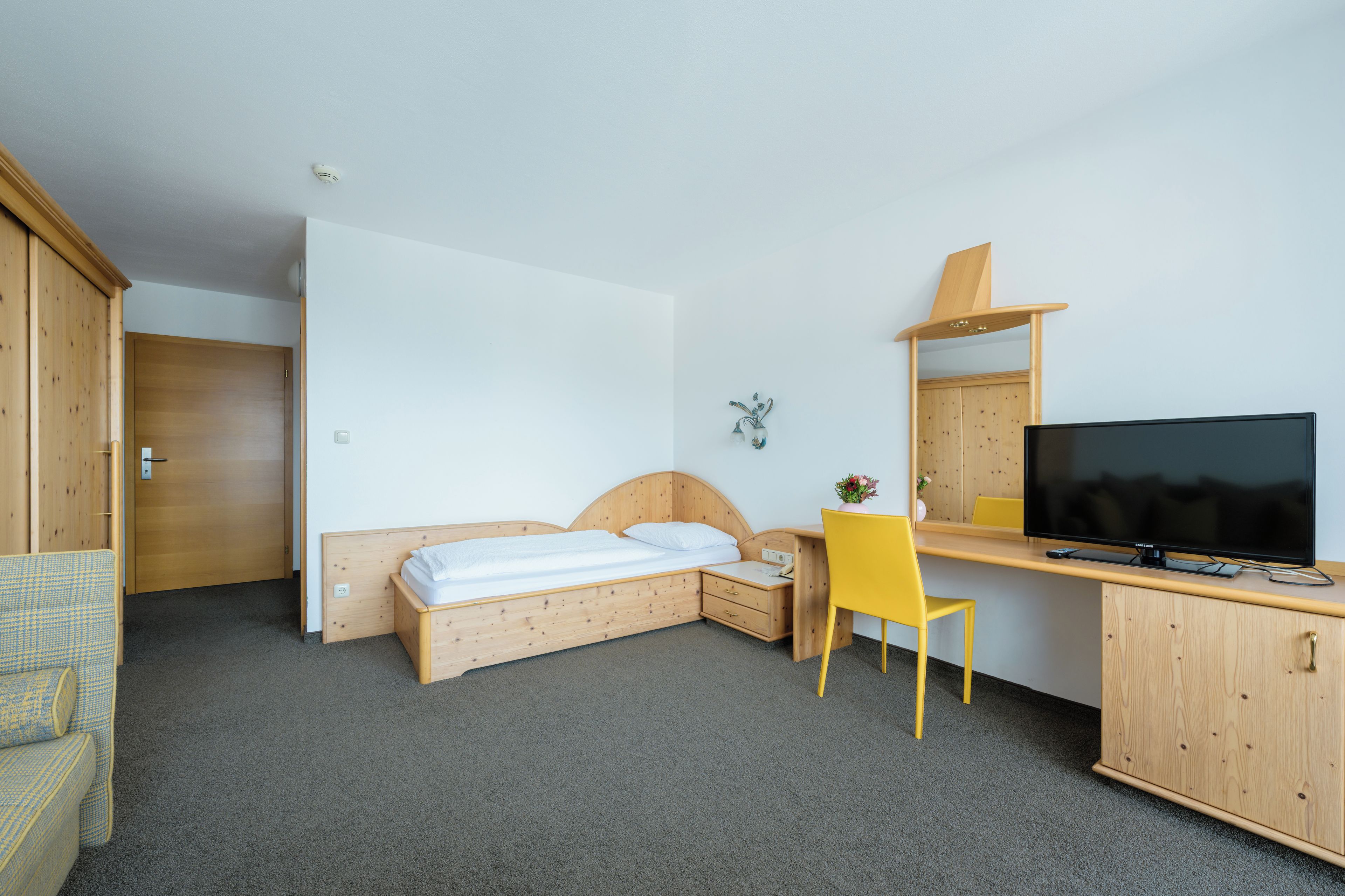 A hotel room with a bed, a desk with a chair, a television, and a wardrobe.