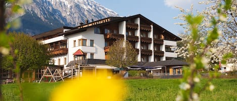 Un hotel de varios pisos con balcones, un telesilla y el paisaje de una montaña al fondo.