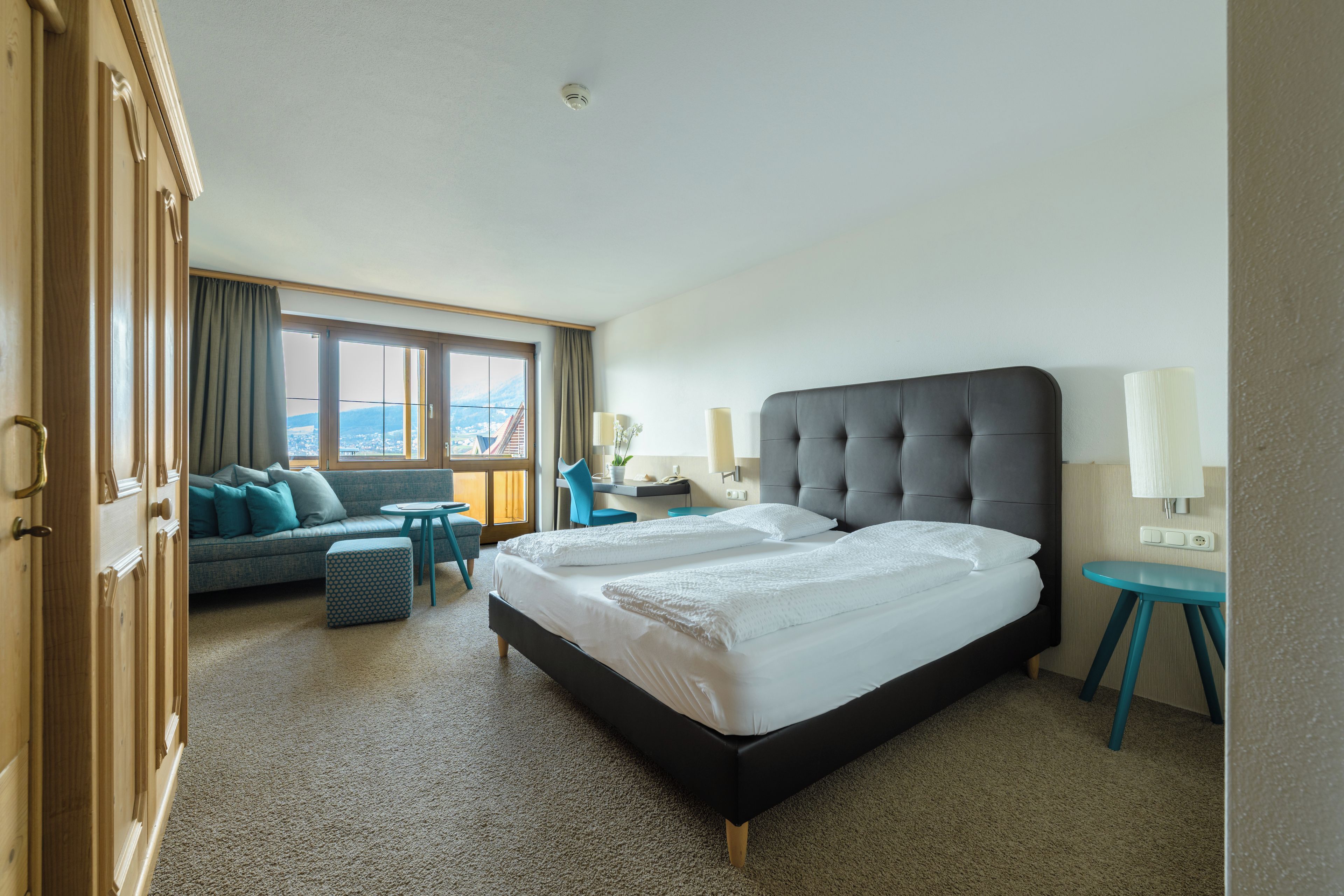 A hotel room with a large bed, a sofa, a small table, and a view of the city.
