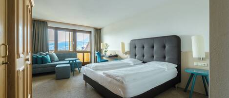 A hotel room with a large bed, a sofa, a small table, and a view of the city.