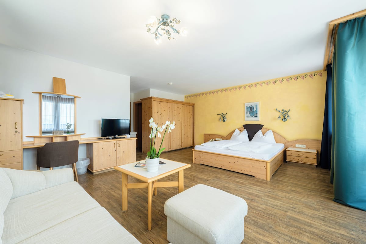 A hotel room with a bed, a desk, a television, a chair, and a small table with a plant.