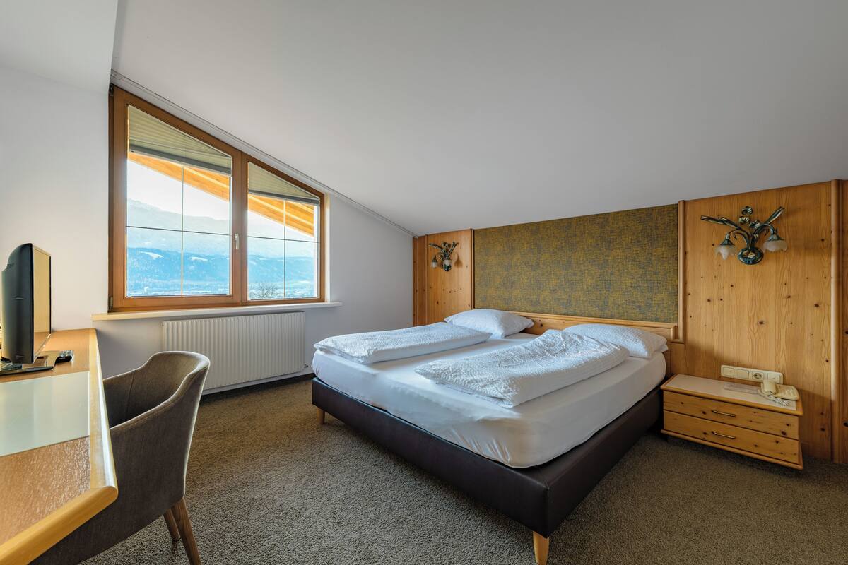 A bedroom with a large bed, a desk, a chair, and a window with a view of mountains.
