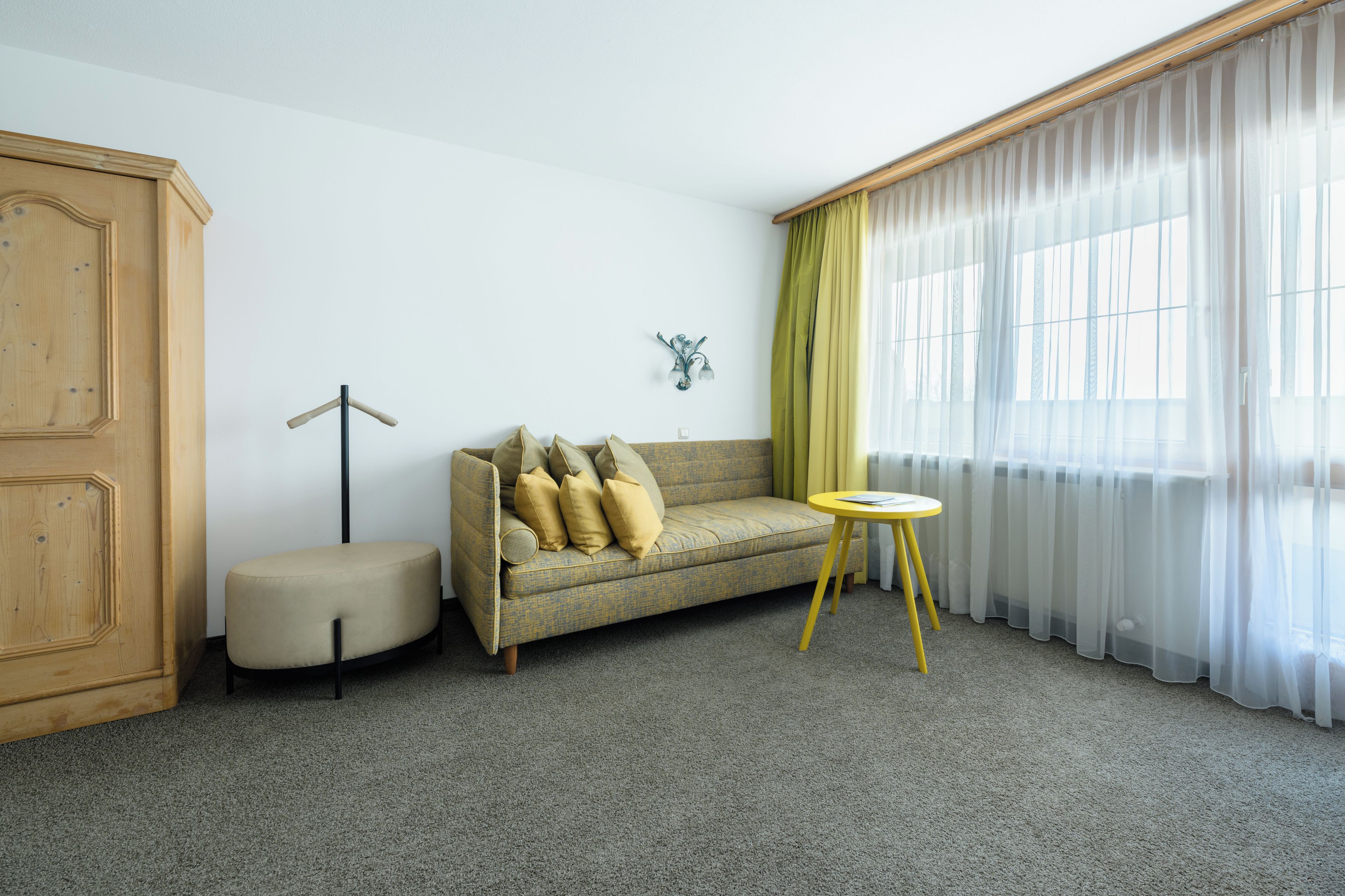 A room with a sofa, a small round table, a cabinet, and a window with sheer curtains.