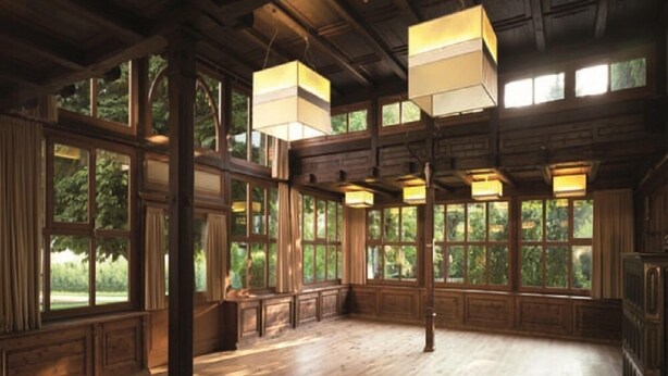 A spacious room with large windows, wooden beams, and hanging lanterns.