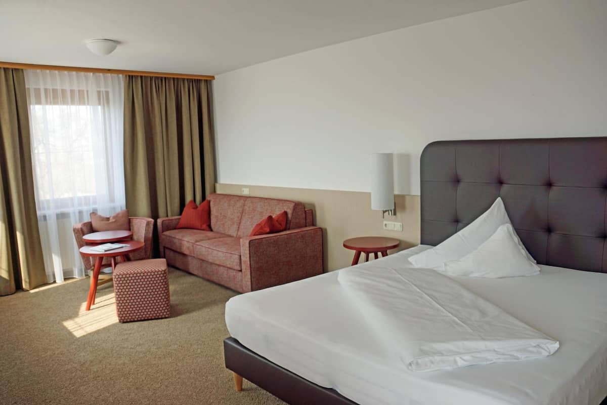 A hotel room with a large bed, a sofa, a small table, and a chair.