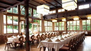 A large dining hall with long tables set for a meal, wooden chairs, and large windows allowing natural light.