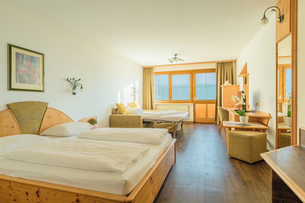 A hotel room with two beds, a desk, a chair, a small table, a mirror, and a window with a view.