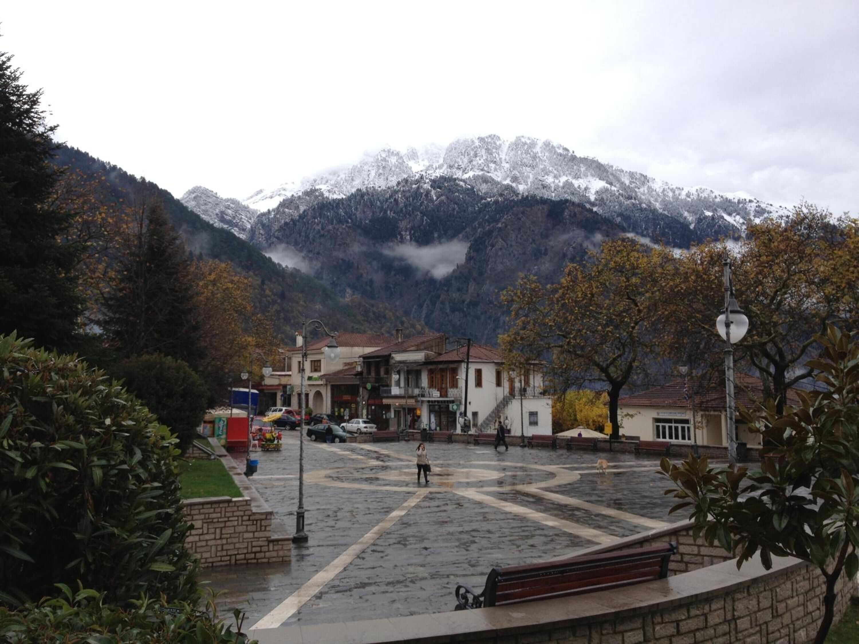 Una plaza rectangular con edificios, bancos y una montaña al fondo.