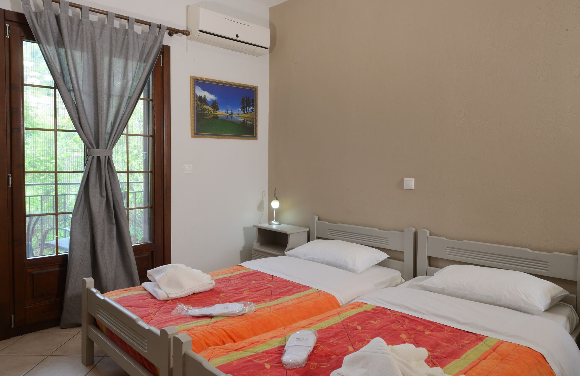 Une chambre d’hôtel avec deux lits, une table de chevet avec une lampe, un tableau au mur et une fenêtre avec des rideaux.