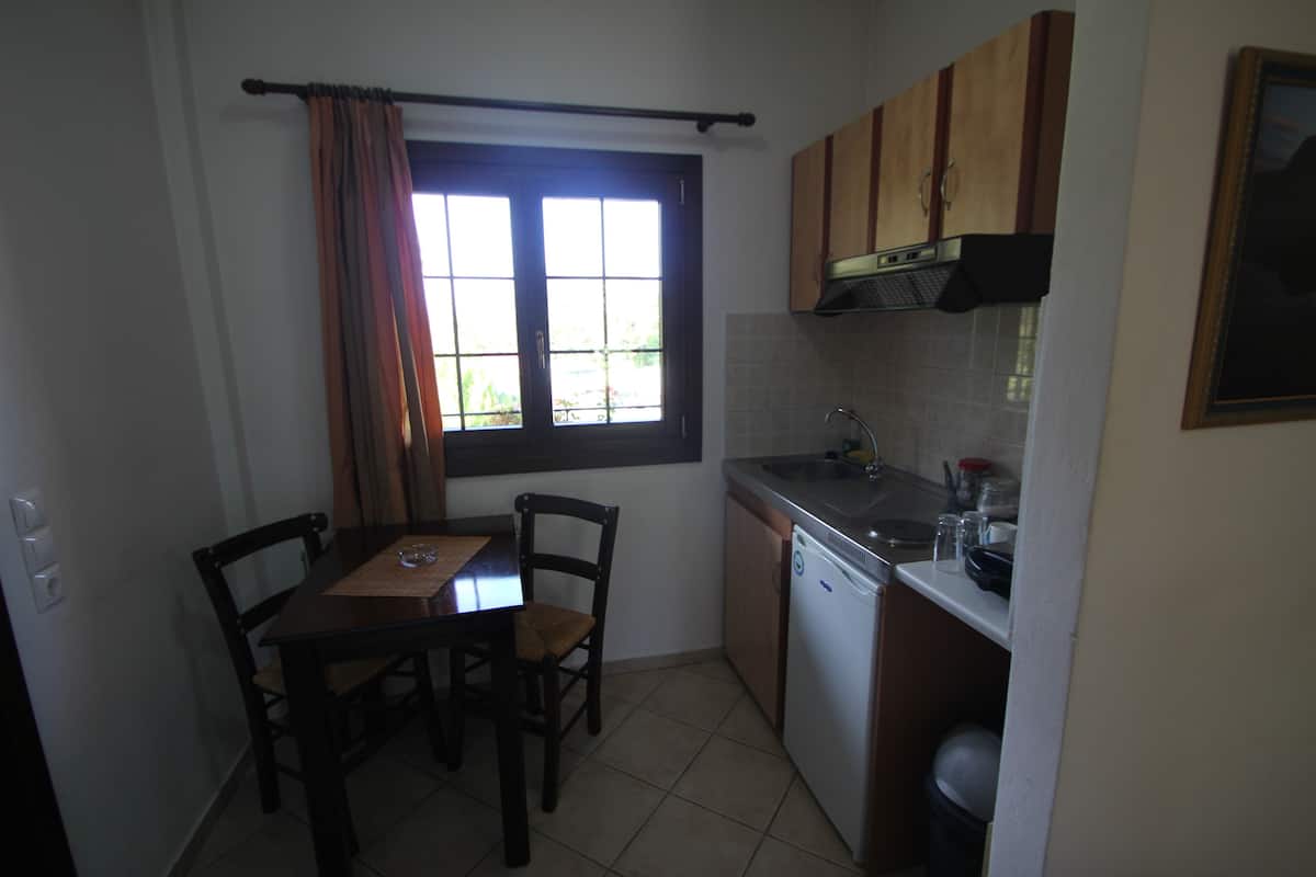 Una cocina compacta con una mesa y sillas, una ventana con cortinas y electrodomésticos básicos.