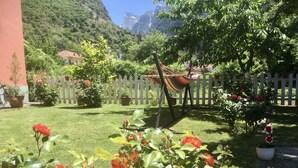 Un jardín con una hamaca, cerca blanca en forma de piquete y montañas al fondo.