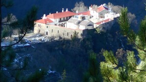 Un edificio grande e histórico con varias secciones y un techo rojo, rodeado de árboles y nieve.